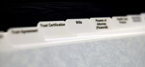 Estate planning documents organized with tabs for Will Power of Attorney and Trust. Visual concept for an estate planning blog discussing the question: If you have a trust do you need a will?